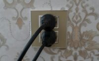 Two black plugs inserted into a gold electrical outlet.